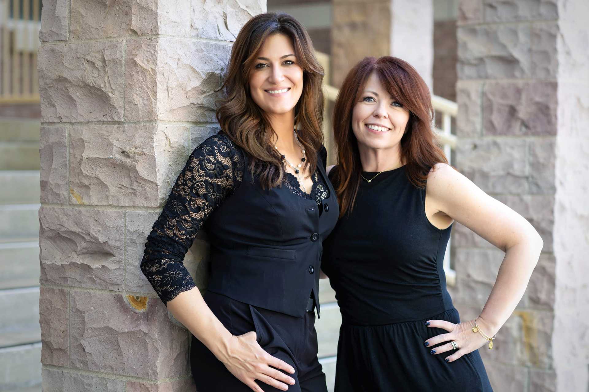 Two women smiling and posing in front of a stone building.
